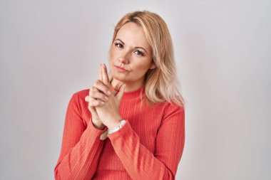 Sarışın bir kadın izole edilmiş arka planda duruyor. Elinde sembolik bir silahla el hareketleriyle cinayet silahlarıyla oynuyor. Kızgın bir yüz. 