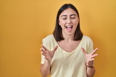 Sarı arka plan üzerine gündelik tişört giyen İspanyol kız kollarını kaldırmış ve gözleri kapalı heyecanla haykırarak başarının çılgınlığını kutluyor. Kazanan konsept 