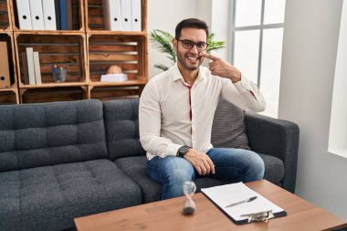 Muayenehanede çalışan sakallı genç bir İspanyol adam. Parmak omuza, gülümsüyor. güzellik konsepti 