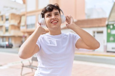 İkili olmayan adam sokakta durup müzik dinliyor.