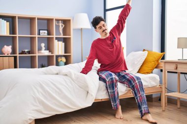 Young caucasian man waking up stretching arms at bedroom