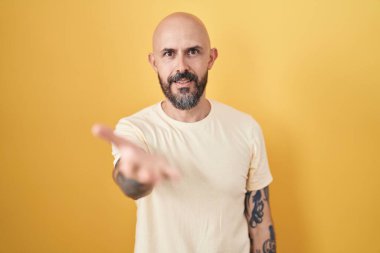 Sarı arka planda dikilen İspanyol dövmeli adam gülümseyen, yardım eli uzatan ve kabul gören.. 