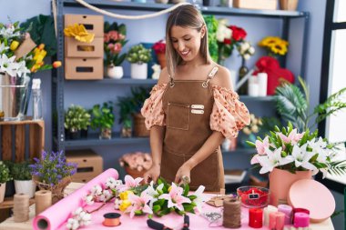 Young beautiful hispanic woman florist make bouquet of flowers at flower shop