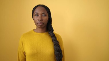 İzole edilmiş sarı arka plan üzerinde ciddi bir ifadeyle duran Afrikalı kadın.