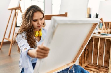 Young beautiful hispanic woman artist looking draw with serious expression at art studio