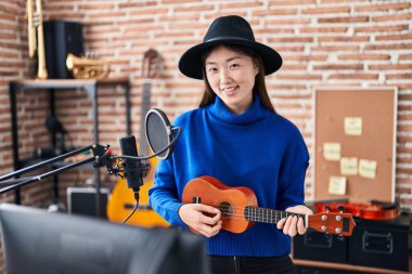 Müzik stüdyosunda ukulele çalarken gülümseyen Çinli kadın müzisyen.