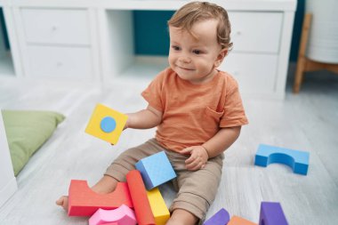 Anaokulunda yerde oturmuş geometri bloklarıyla oynayan sevimli sarışın çocuk.