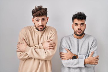 Beyaz arka planda duran genç homoseksüel çift yüzünde üzgün ve şok ifadesiyle kış soğuğu için titriyor ve donuyor. 