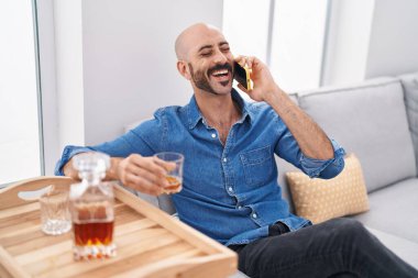 Genç İspanyol adam akıllı telefonda konuşuyor. Evde viski içiyor.