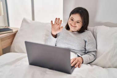 Down sendromlu genç bir kadın yatak odasında video görüşmesi yapıyor.