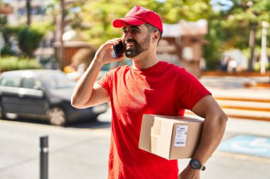 Genç İspanyol kurye caddedeki akıllı telefon paketinden konuşuyor.