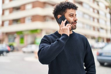 Genç Arap adam gülümsüyor, kendinden emin bir şekilde caddedeki akıllı telefondan konuşuyor.