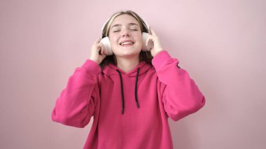 Genç sarışın kadın müzik dinliyor ve pembe arka planda dans ediyor.