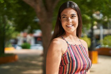 Genç, güzel, İspanyol bir kadın, gülümsüyor. Parkta kendine güveniyor.