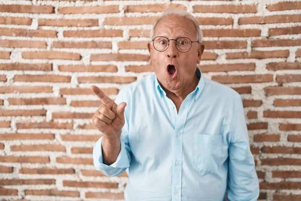 Starší Muž Šedivými Vlasy Stojící Nad Cihlovými Zdmi Překvapený Ukazováčkem — Stock fotografie