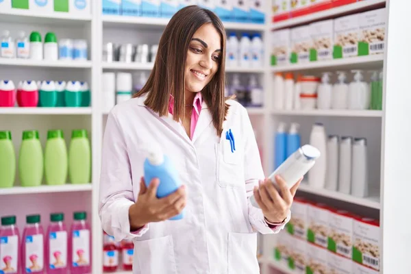 Young Beautiful Hispanic Woman Pharmacist Holding Shampoo Bottles Pharmacy — Stok fotoğraf