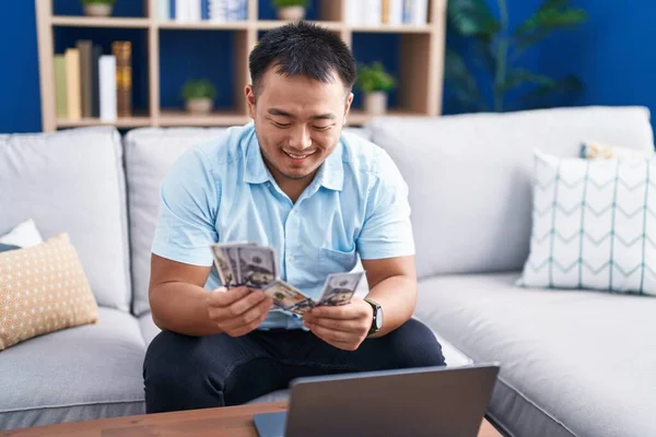 Young Chinese Man Using Laptop Counting Dollars Home — Stock Photo, Image