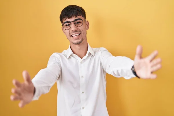 Mladý Hispánec Stojí Nad Žlutým Pozadím Dívá Kameru Otevřenou Náručí — Stock fotografie