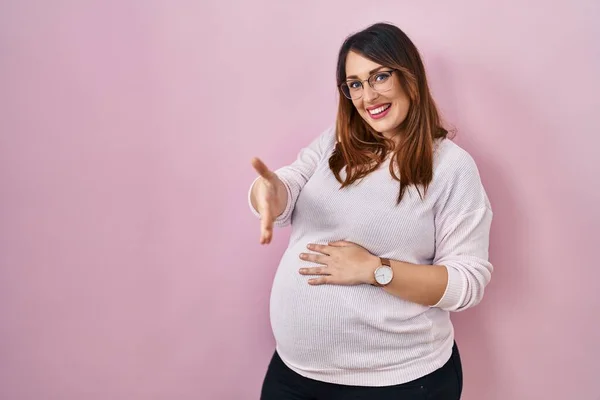 Zwangere Vrouw Staat Roze Achtergrond Glimlachend Vriendelijk Aanbieden Van Handdruk — Stockfoto