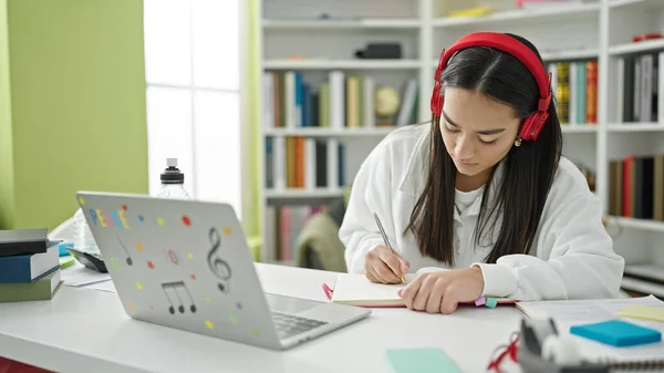 ラップトップとヘッドフォンを使用して若い美しいヒスパニック女性学生大学の教室でノートを書きます — ストック写真