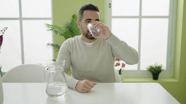 Young Hispanic Man Drinking Water Sitting Table Home — Stockfoto