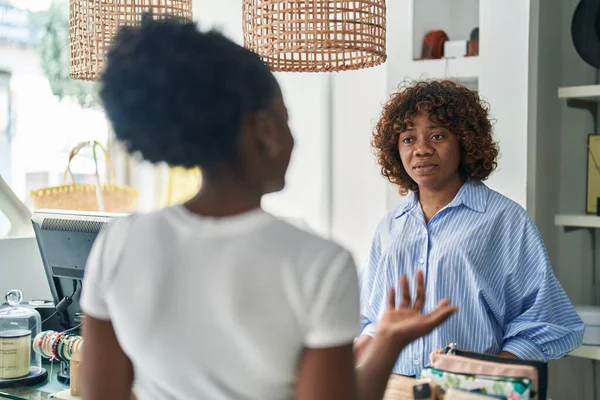 African american women shop assistant and customer speaking at clothing store