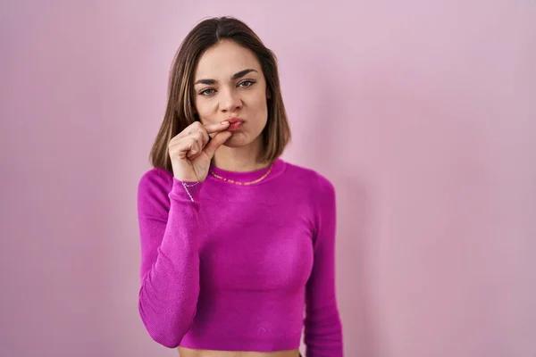 ピンクの背景の口と唇の上に立つヒスパニック系の女性は指でZipとしてシャットダウンします 秘密裏に黙ってタブーを語る — ストック写真
