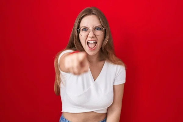 Mladá Běloška Stojící Nad Červeným Pozadím Ukazuje Kameru Nespokojeně Frustrovaně — Stock fotografie