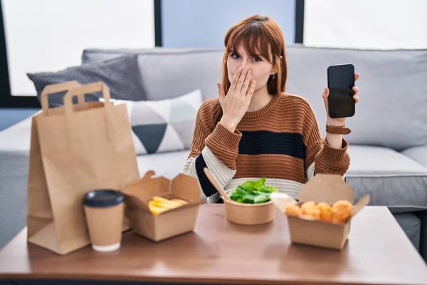 stock image Young beautiful woman eating delivery food at the living room covering mouth with hand, shocked and afraid for mistake. surprised expression 