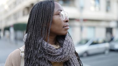 African woman standing from the side with serious expression wearing glasses at street