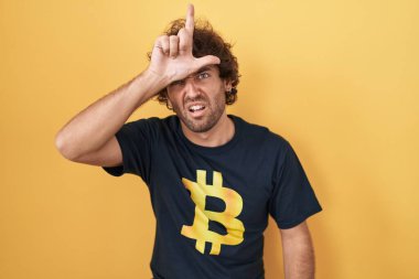 İspanyol genç adam bitcoin tişört giyiyor. Alnında parmakları olan insanlarla dalga geçiyor. Ezik hareketler yapıyor, alay ediyor ve hakaret ediyor.. 