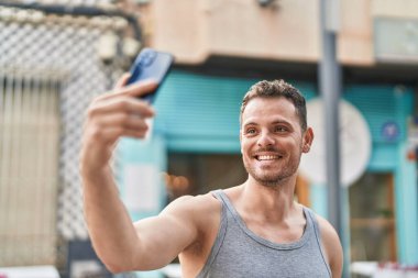 Young hispanic man smiling confident making selfie by the smartphone at street