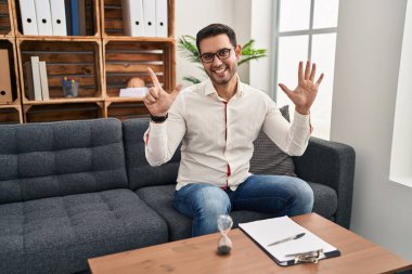 Danışma ofisinde çalışan sakallı, genç İspanyol bir adam yedi numaralı parmaklarını gösterip işaret ederken kendinden emin ve mutlu bir şekilde gülümsüyor.. 