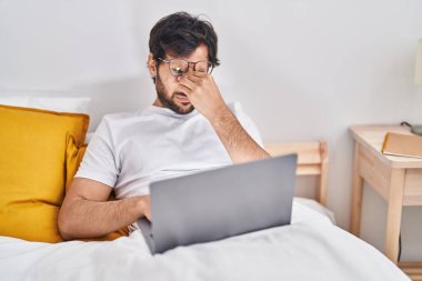 Genç İspanyol adam yatak odasında dizüstü bilgisayar kullanmaktan yoruldu.