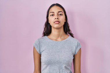 Pembe arka plan üzerine gündelik tişört giyen genç Brezilyalı kadın yüzünde ciddi bir ifadeyle rahatlamış. Basit ve doğal bir şekilde kameraya bakıyorsun.. 
