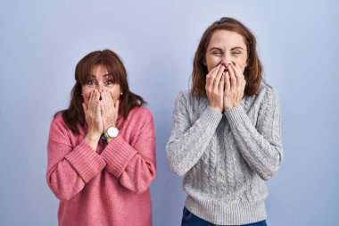 Anne ve kızı mavi arka planda gülüyor ve utanıyor kıkırdıyor ağızlarını ellerle, dedikodularla ve skandallarla örtüyor. 