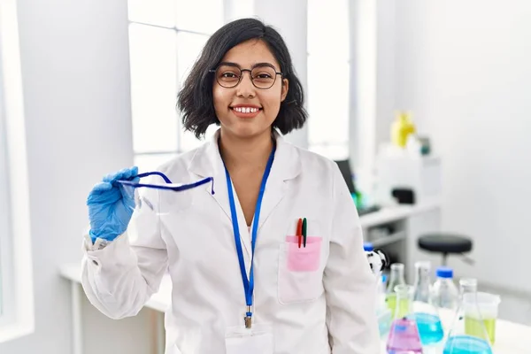 Joven Mujer Hispana Trabajando Laboratorio Científico Sosteniendo Gafas Seguridad Con —  Fotos de Stock