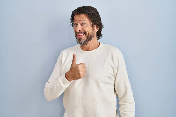 青い背景にカジュアルなセーターを着たハンサムな中年男性が手で幸せな親指アップジェスチャーを行います 成功を示すカメラを見ると — ストック写真
