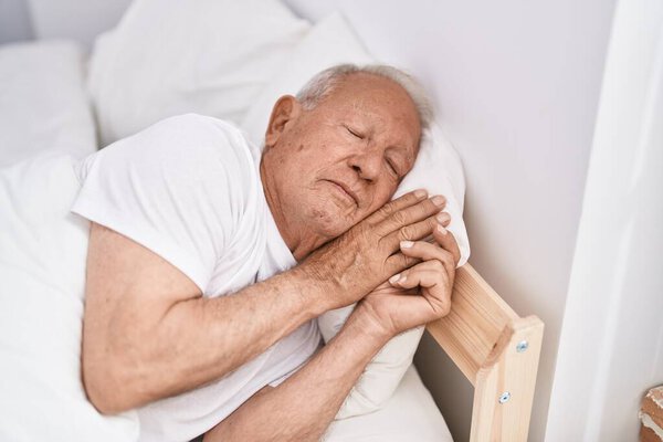 Старший седой мужчина лежит на кровати и спит в спальне.