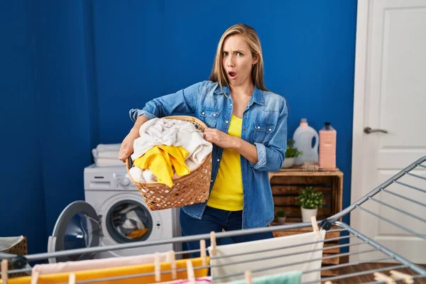 Young Blonde Woman Holding Laundry Basket Shock Face Looking Skeptical — Stock Photo, Image