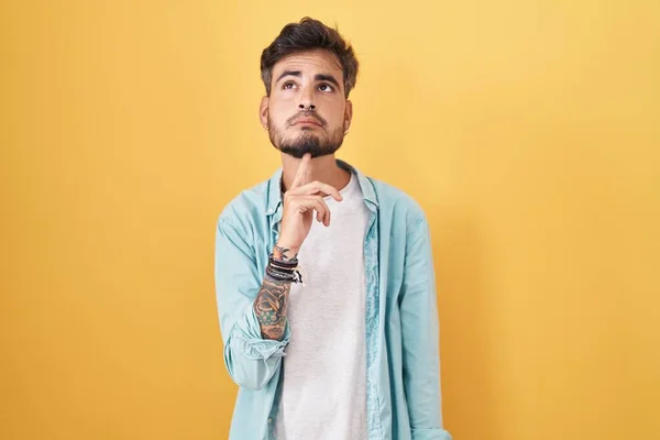 Jovem Hispânico Com Tatuagens Sobre Fundo Amarelo Pensando Concentrou Dúvida — Fotografia de Stock