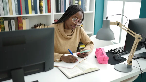 アフリカの女性は図書館大学のスマートフォンでノートを取るコンピュータを使って — ストック写真