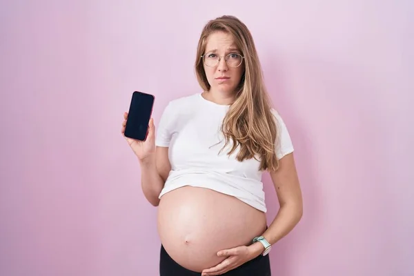 Jonge Zwangere Vrouw Tonen Buik Houden Smartphone Sceptisch Nerveus Fronsen — Stockfoto