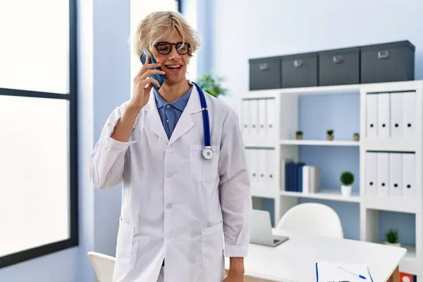 Young Blond Man Doctor Smiling Confident Talking Smartphone Clinic — Stockfoto