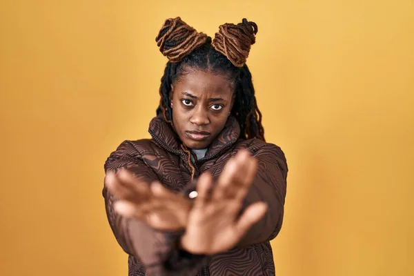 黄色の背景拒絶表現の上に立っている編組の髪を持つアフリカの女性腕と手のひらを横断負の記号を行う 怒っている顔 — ストック写真