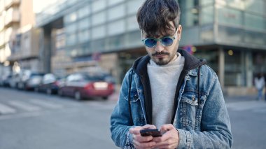 Sokak ortasında güneş gözlüğü takan genç bir İspanyol akıllı telefon kullanıyor.