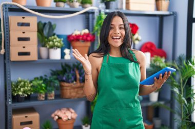 Çiçekçi dükkanında çalışan esmer kadın elinde tabletle çılgınlığı kutluyor ve başarı için hayrete düşüyor.. 