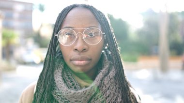 African woman standing with serious expression wearing glasses at street