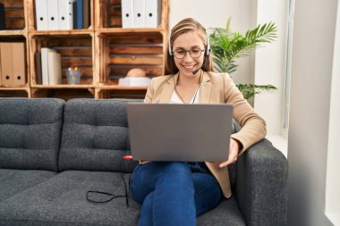 Çevrimiçi randevuda çalışan genç sarışın kadın pozitif ve mutlu görünüyor. Dişlerini gösteren bir gülümsemeyle ayakta duruyor ve gülümsüyor. 