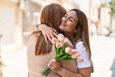 Mother and daughter hugging each other holding bouquet of flowers at street